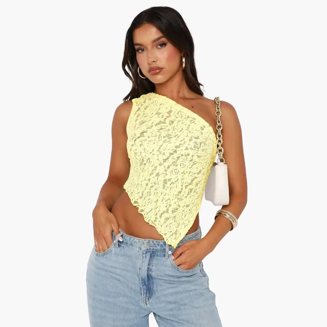 Lace one-shoulder top in pale yellow with an asymmetrical hem, styled with light-wash jeans.