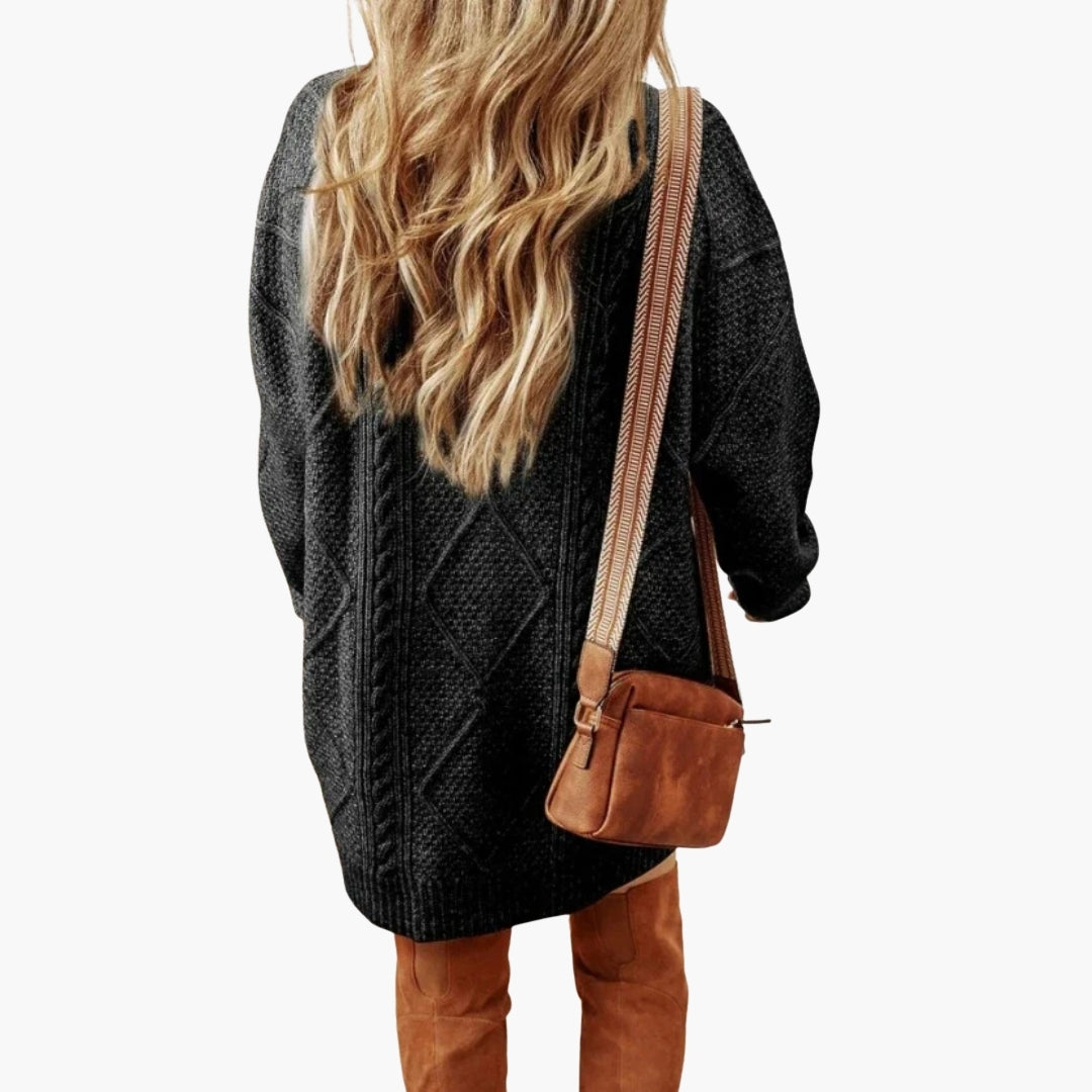 Women's oversized black knit dress with cable detailing and ribbed edges, paired with a brown suede crossbody bag.