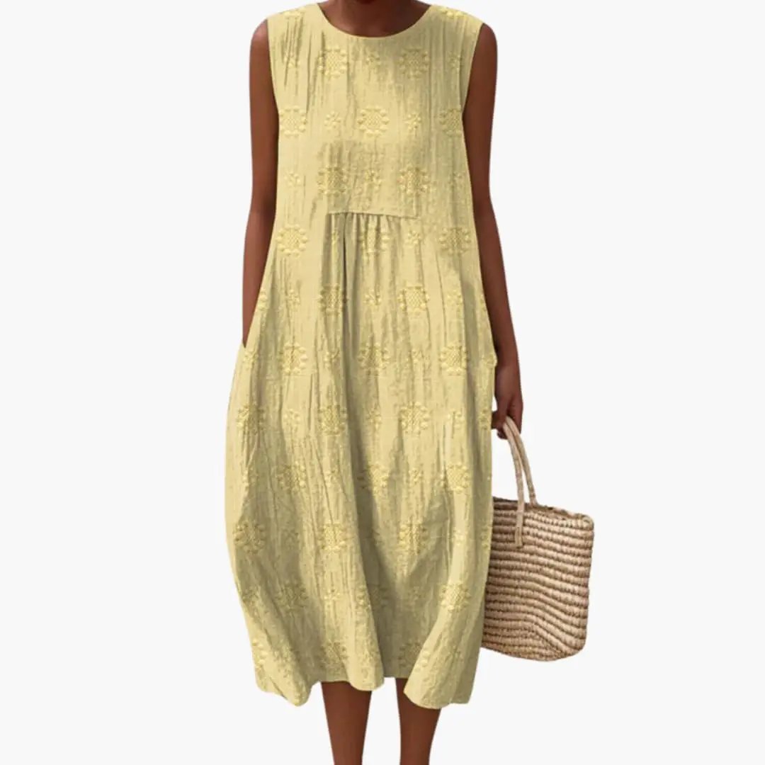 Women's sleeveless yellow maxi dress with side pockets and embroidered floral pattern, paired with a straw tote.