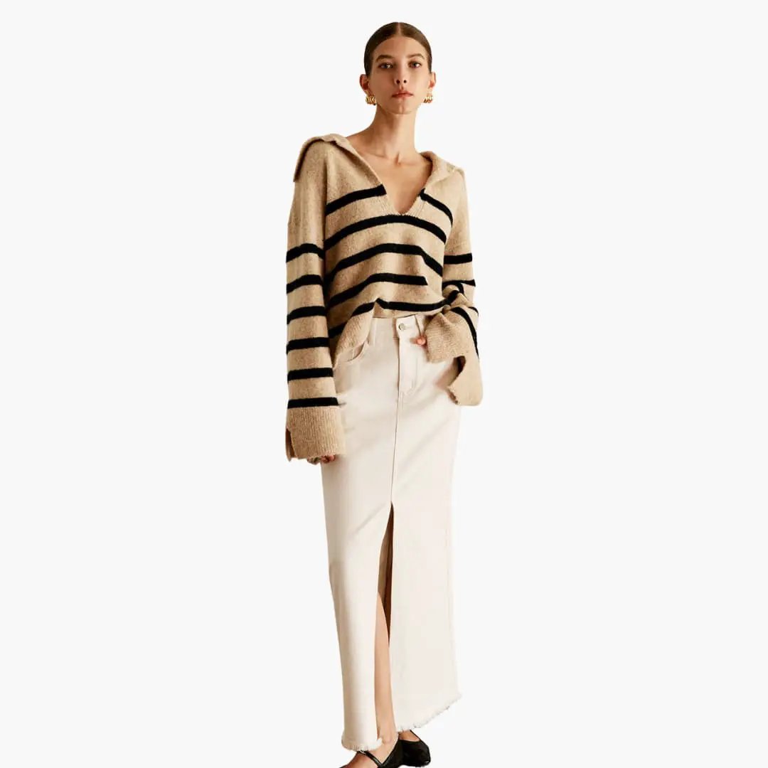 Women's pullover with V-neck; oversized beige knit with black stripes, paired with a cream skirt with front slit.