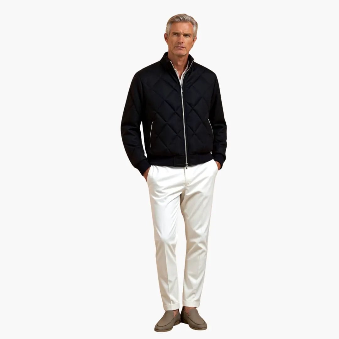 Men's black quilted jacket with zip front; model wearing white trousers and beige loafers.